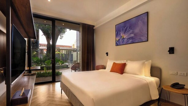 A hotel room with a large bed, a flat-screen TV, a small table, and a view of the outdoors. - Red Door (Bangkok)