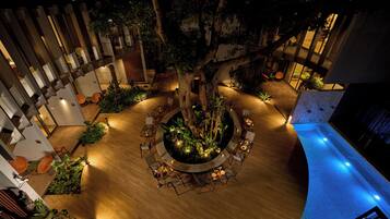 Un espace extérieur circulaire aménagé en coin salon, avec un arbre au centre, entouré d’un sol en bois et de chaises.