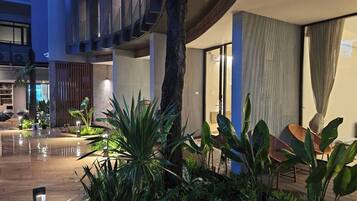 A modern hotel lobby with a wet floor, indoor plants, a large tree trunk, and a seating area with chairs.