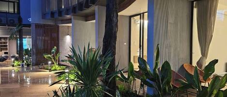 Un moderno vestíbulo de hotel con suelo mojado, plantas de interior, un gran tronco de árbol y una zona de estar con sillones.