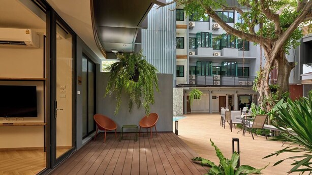 An outdoor deck area with wooden flooring, seating, and a large tree providing shade. - Red Door (Bangkok)