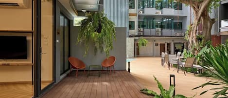 An outdoor deck area with wooden flooring, seating, and a large tree providing shade.
