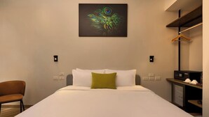 A hotel room with a bed, a single green pillow, a chair, a wall-mounted artwork, and a small table with a microwave. - Red Door (Bangkok)