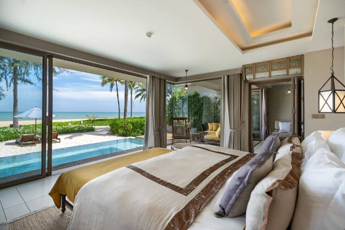 A bedroom with a large bed, a view of the beach, and a pool.