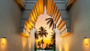 A corridor with a view of palm trees and a sunset. - Devasom Khao Lak Beach Resort & Villas (Takua Pa)