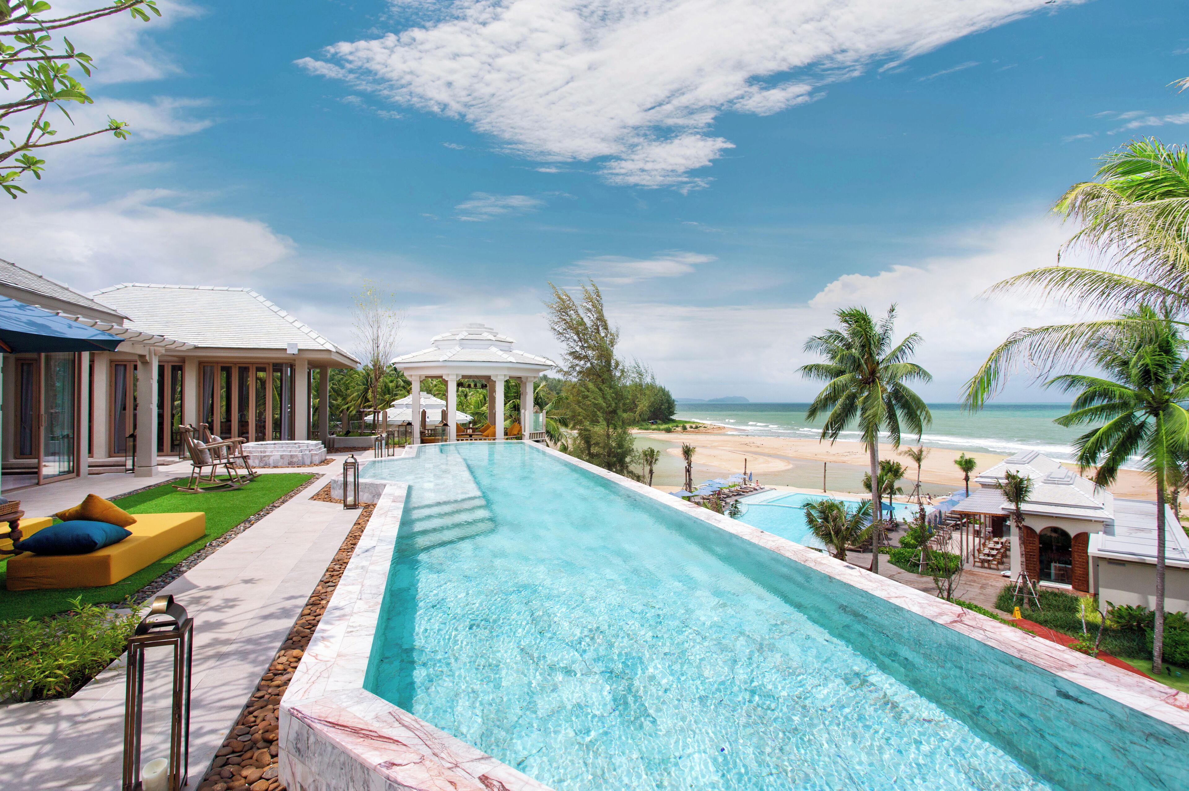 Una piscina con vista a la playa, sillas de descanso y palmeras.