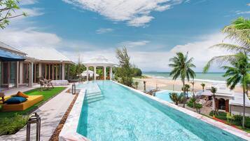 Una piscina con vista a la playa, sillas de descanso y palmeras.