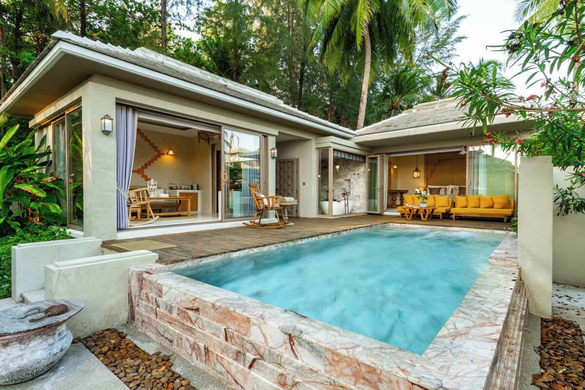 A modern house with a swimming pool, outdoor seating, and a patio area surrounded by lush greenery.