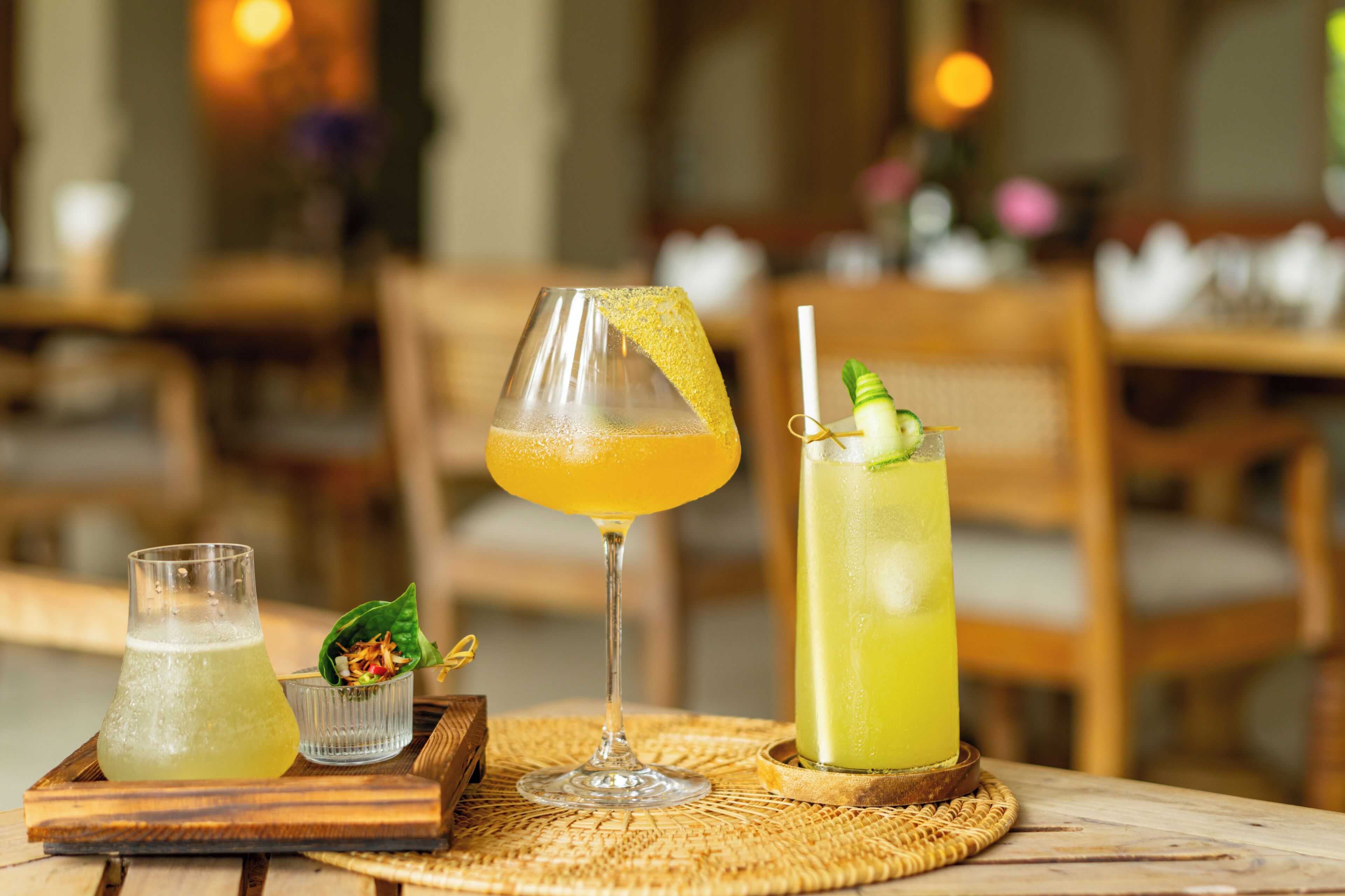 A table with three drinks, a wooden tray, and a woven placemat.