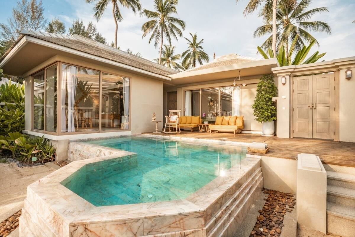 A modern house with a swimming pool, outdoor seating, and palm trees.