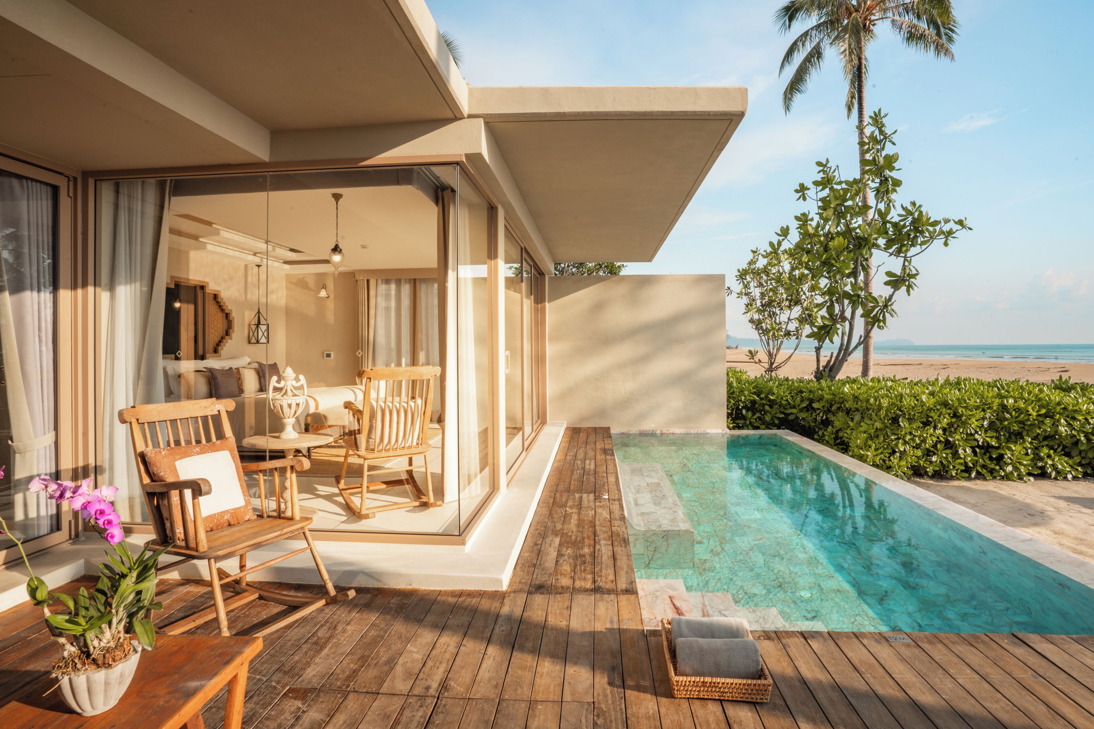 A wooden deck with a pool, outdoor furniture, and a view of the beach.