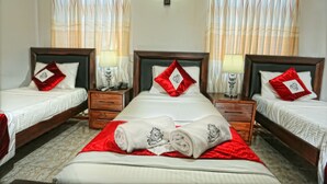 A hotel room with two single beds, each with a wooden headboard, white bedding, and red pillows. There are two bedside tables with lamps, and the room has a tiled floor. - Asian Grand Hotel (Negombo)