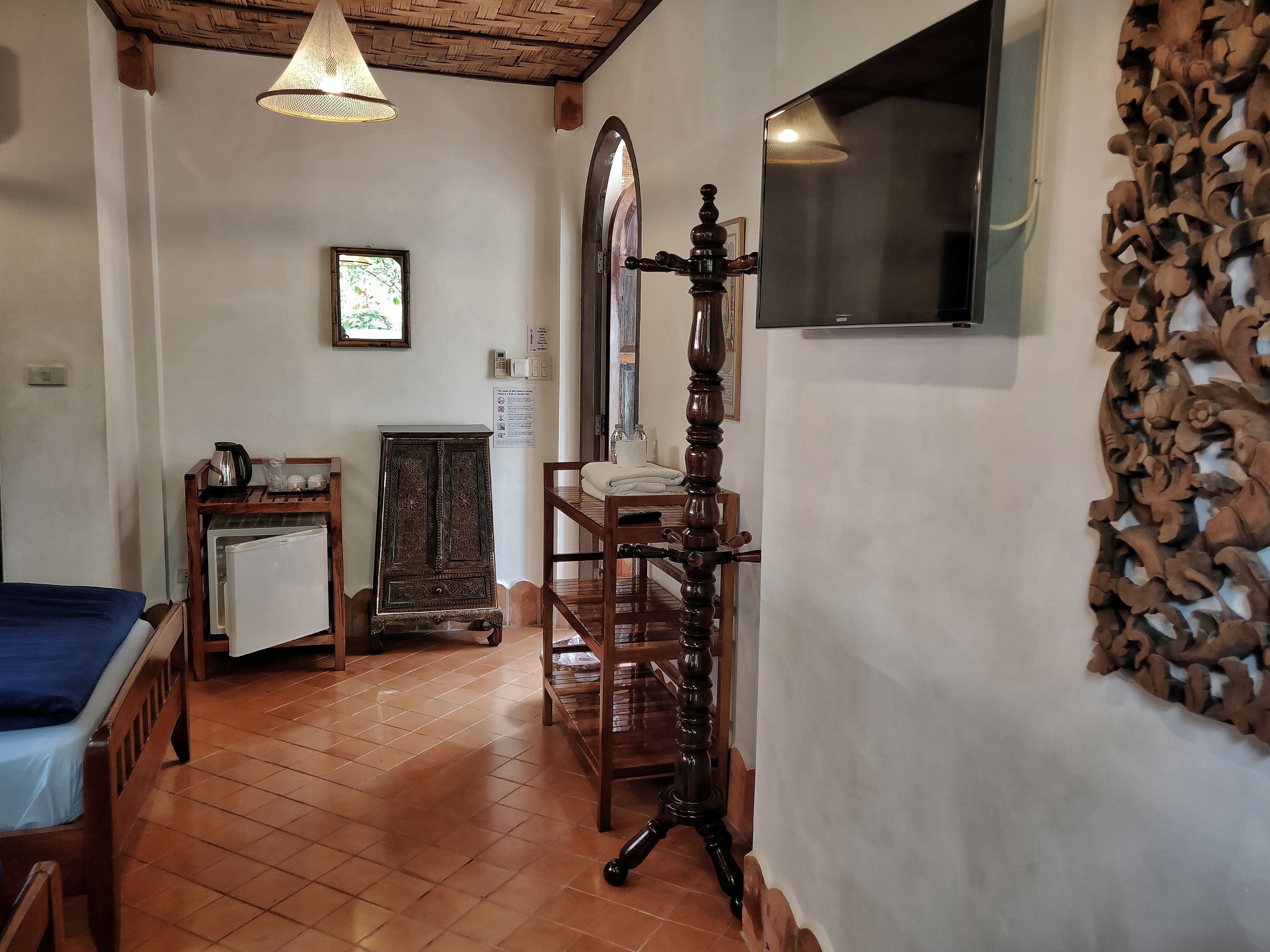A room with a bed, a wooden cabinet, a wooden chair, a wooden table, a wall-mounted TV, and a decorative wall piece.