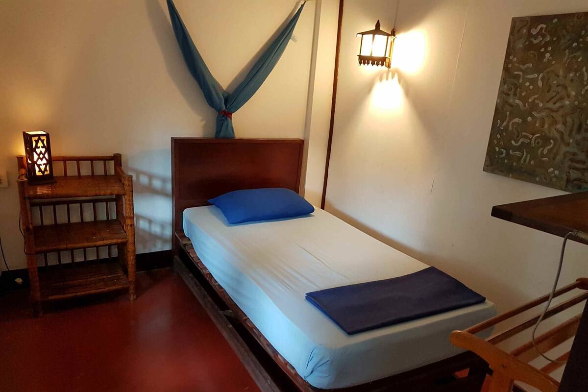Una habitación con una cama de madera, una mesita de noche, una lámpara de pared y un cuadro.