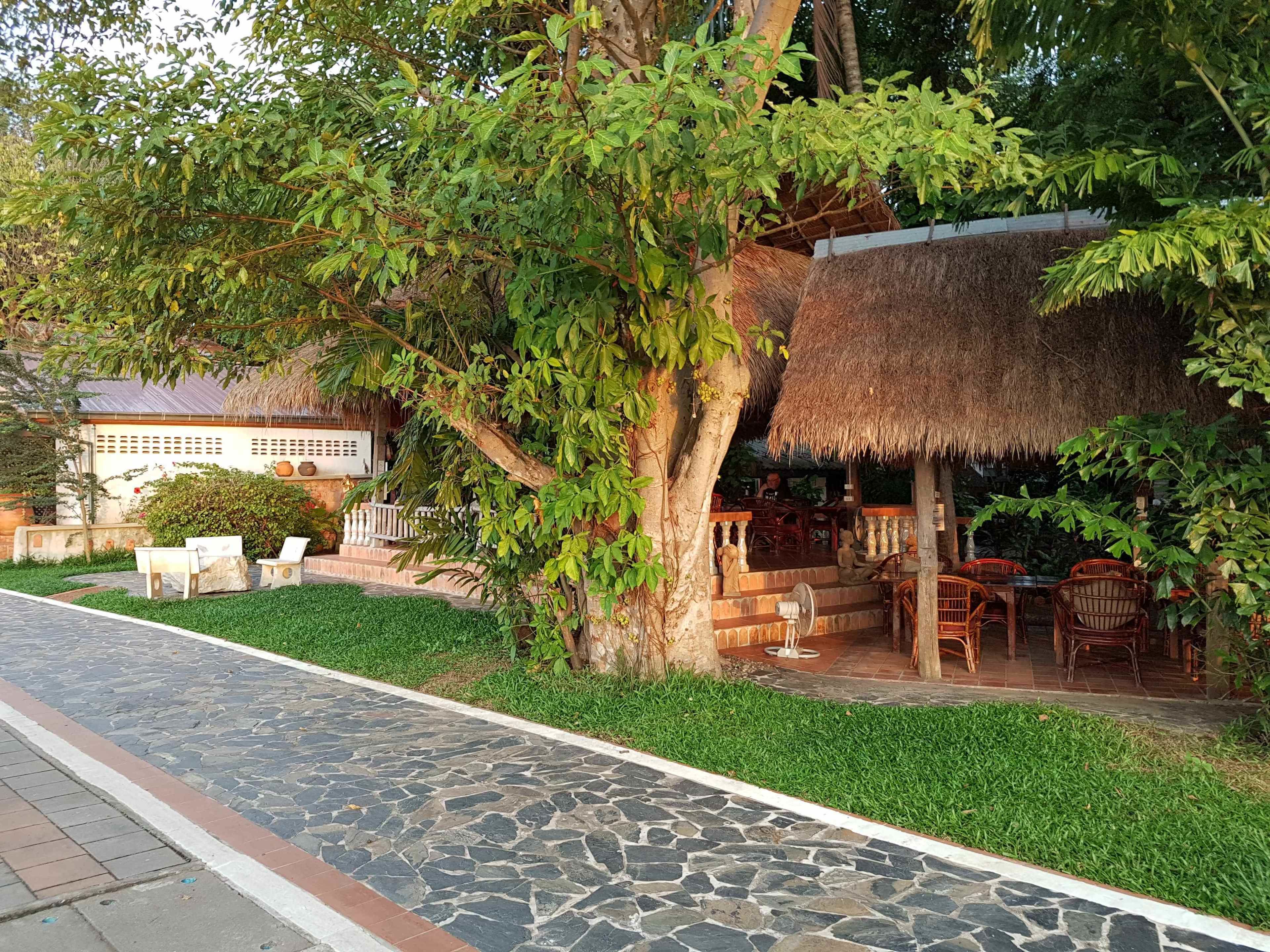 A patio area with stone flooring, outdoor seating, and a thatched-roof structure.
