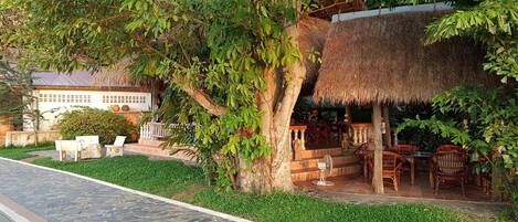 A patio area with stone flooring, outdoor seating, and a thatched-roof structure.