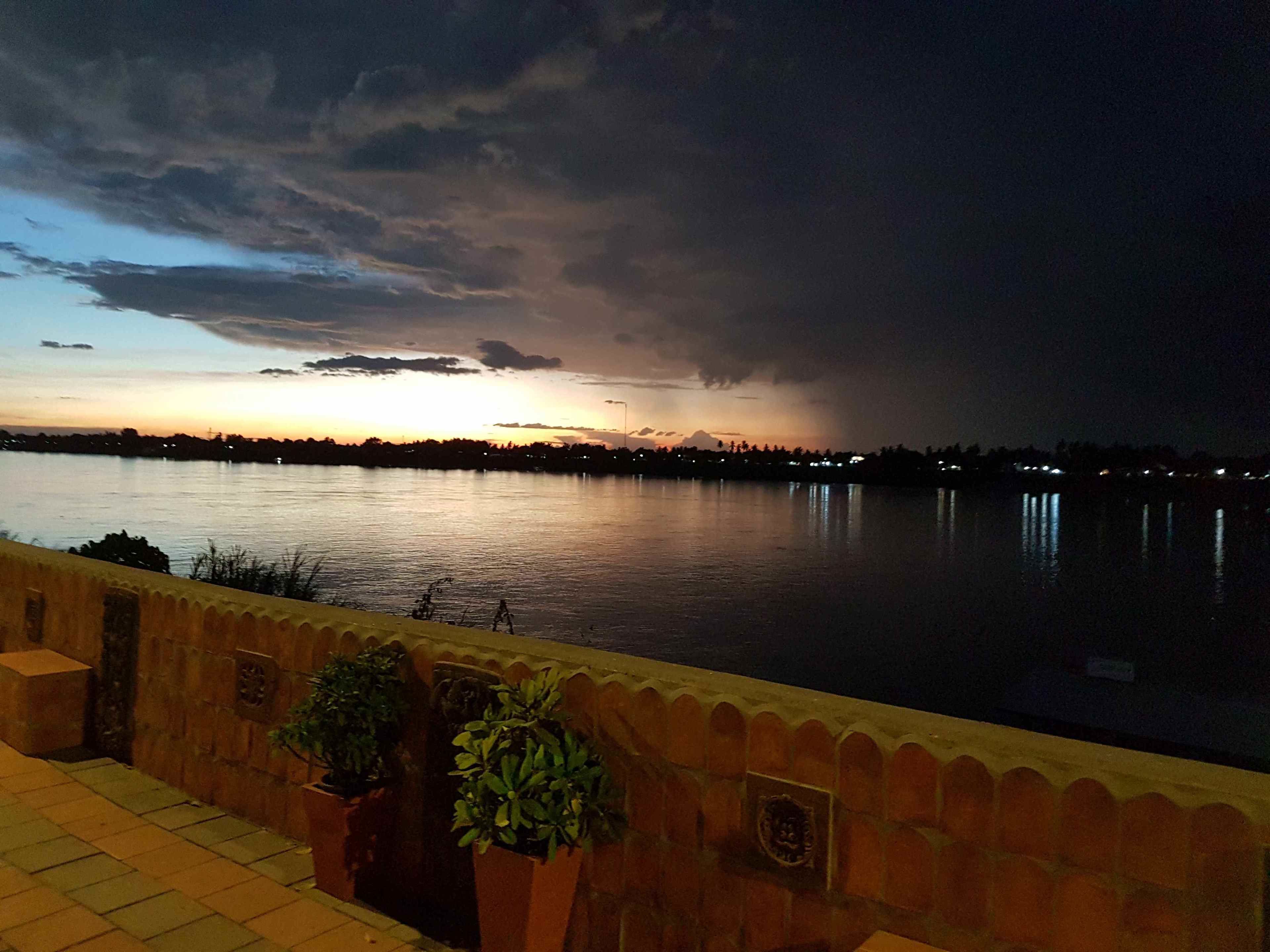 A nighttime view of a calm body of water with a distant city skyline and a cloudy sky.