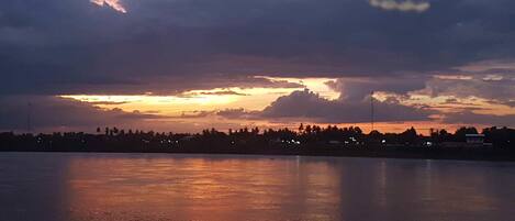 Una masa de agua tranquila que refleja el cielo durante el atardecer, con una orilla lejana y un letrero que dice "Gala Bar".