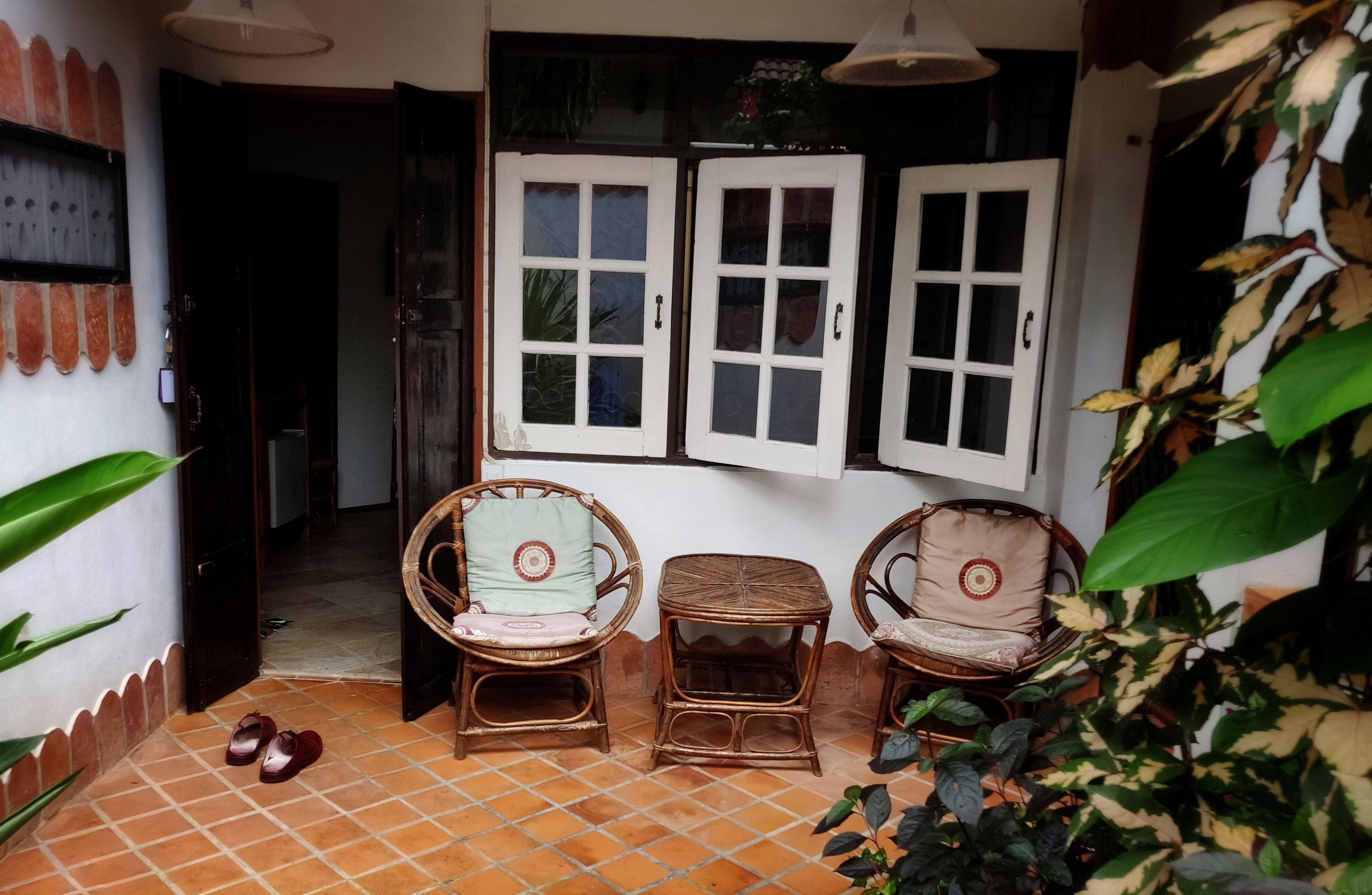 A cozy room with two wicker chairs, a small table, and a window with white shutters.