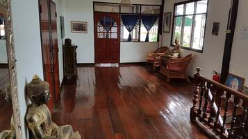 A room with wooden flooring, a Buddha statue, wicker chairs, and a staircase.