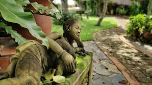 Eine Gartenstatue eines liegenden Menschen, im Vordergrund ein großes Blatt.