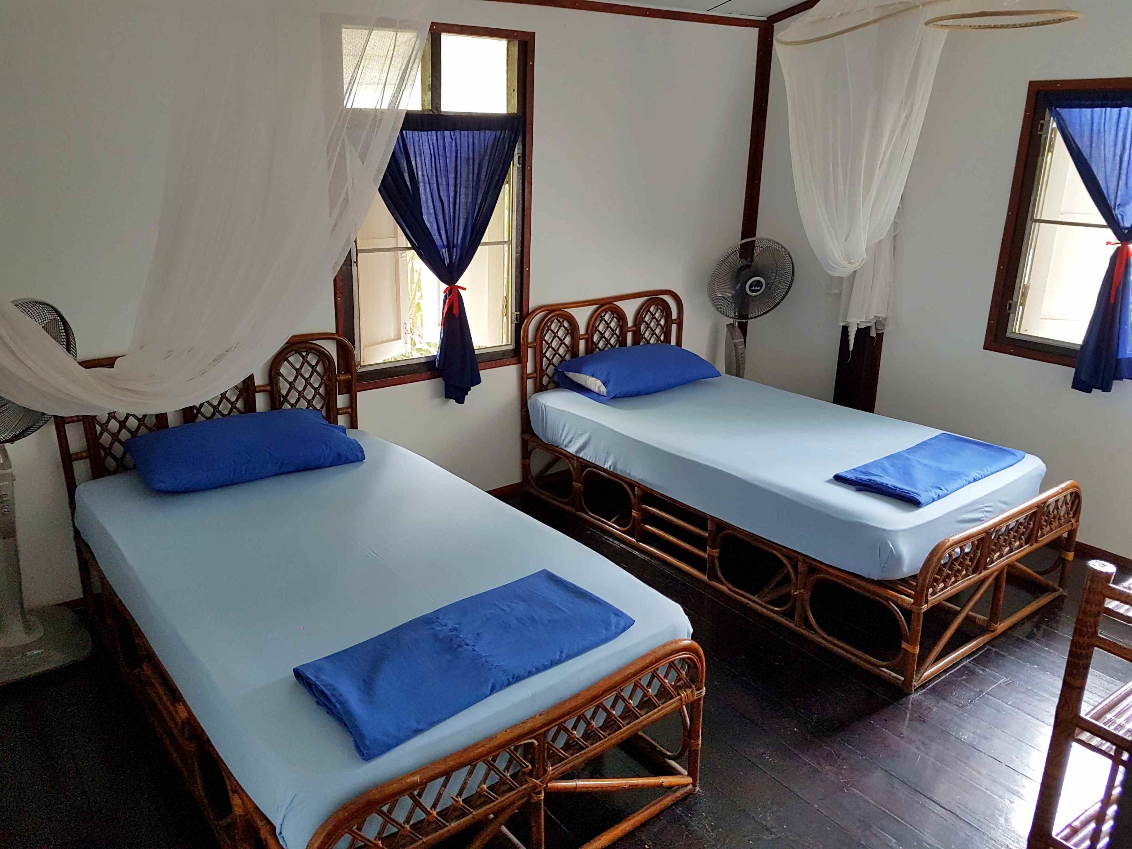 Dos camas de madera con ropa de cama azul y cortinas blancas.
