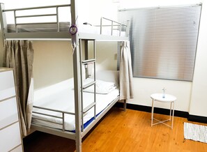 Quarto com beliche, uma pequena mesa e janela com persianas.