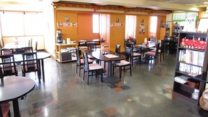 A restaurant with multiple tables and chairs, a coffee machine, and a bookshelf with books and decorative items.