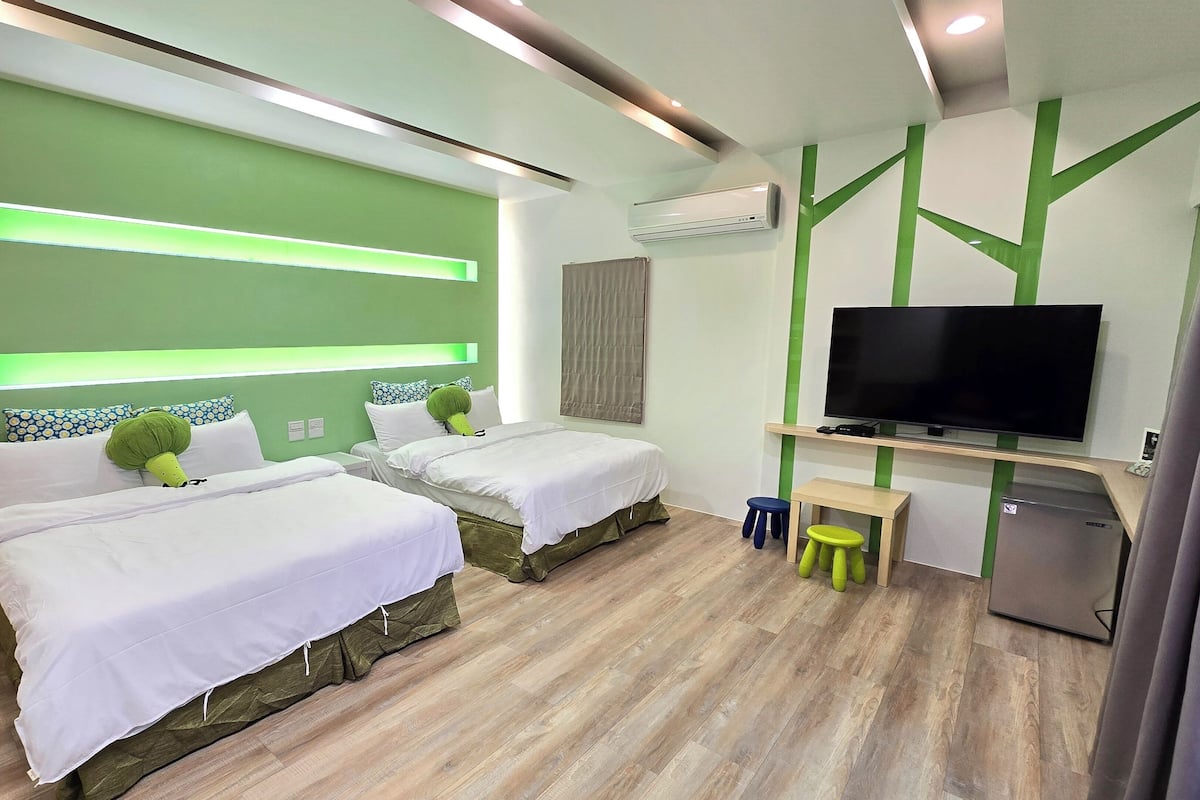 Habitación de hotel con dos camas, televisión, escritorio y un taburete pequeño.