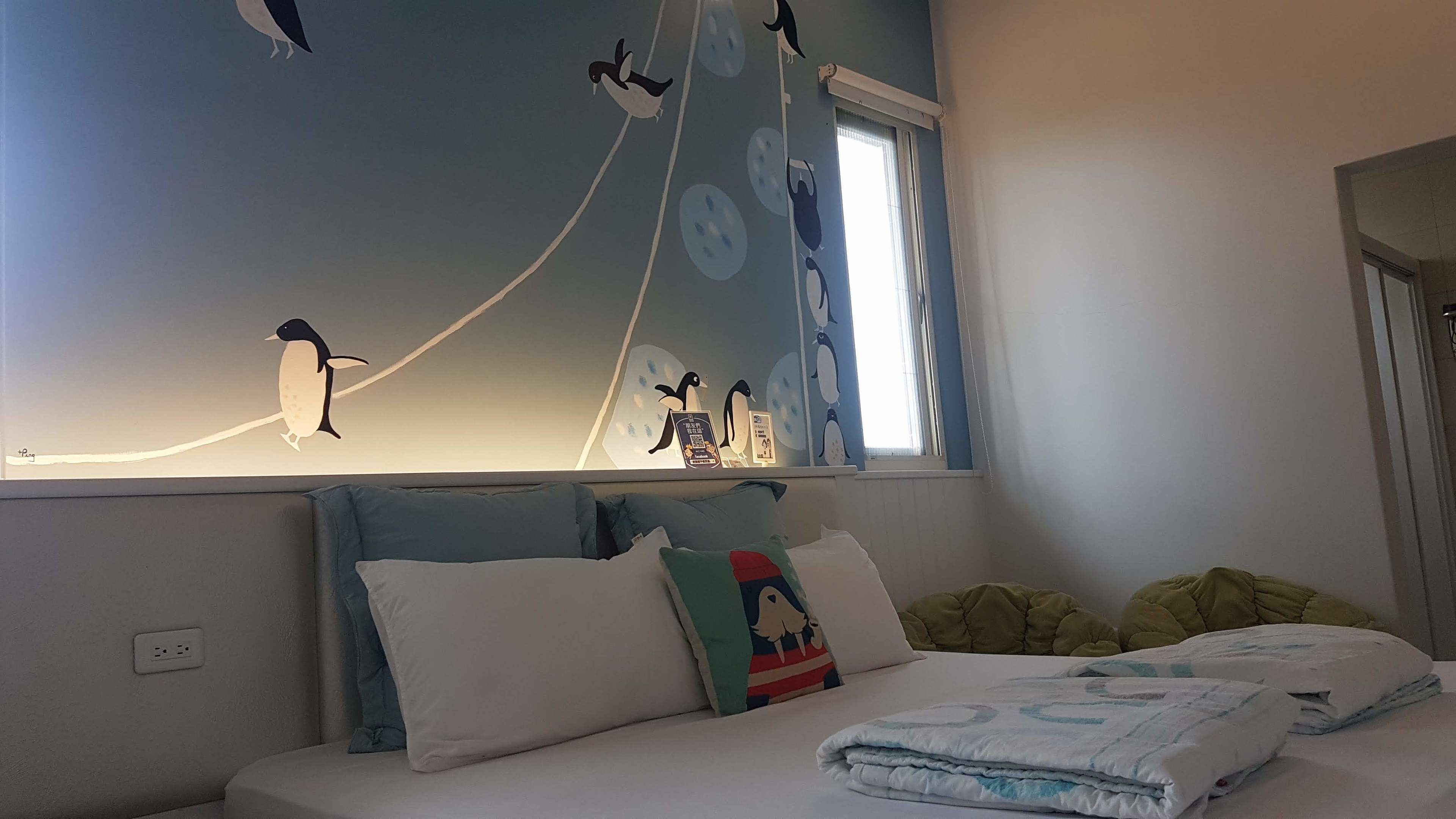 A bedroom with a bed, pillows, a window, and a wall with penguin decorations.