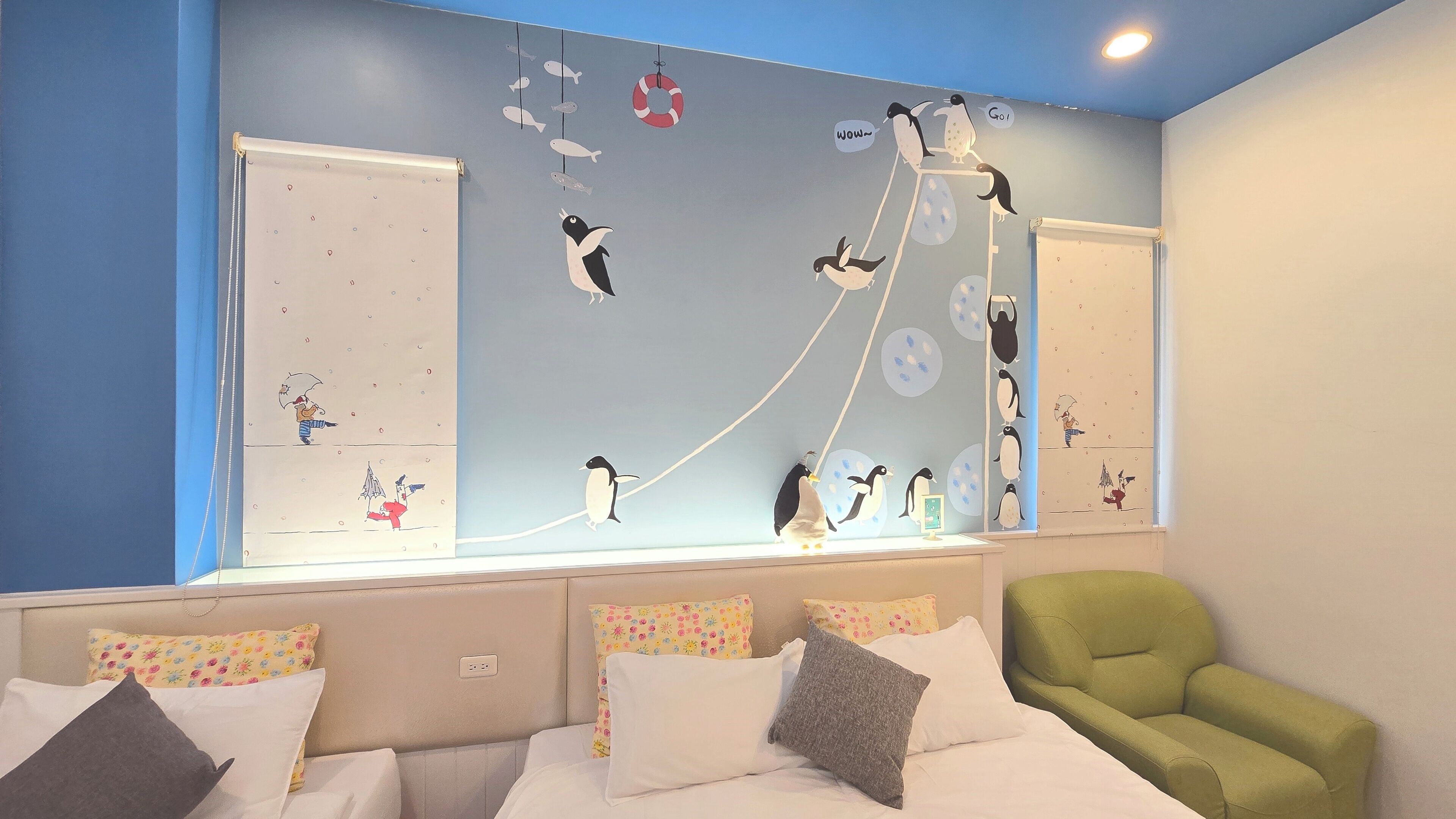 A children's room with a large wall mural of penguins, a green armchair, and a bed with multiple pillows.