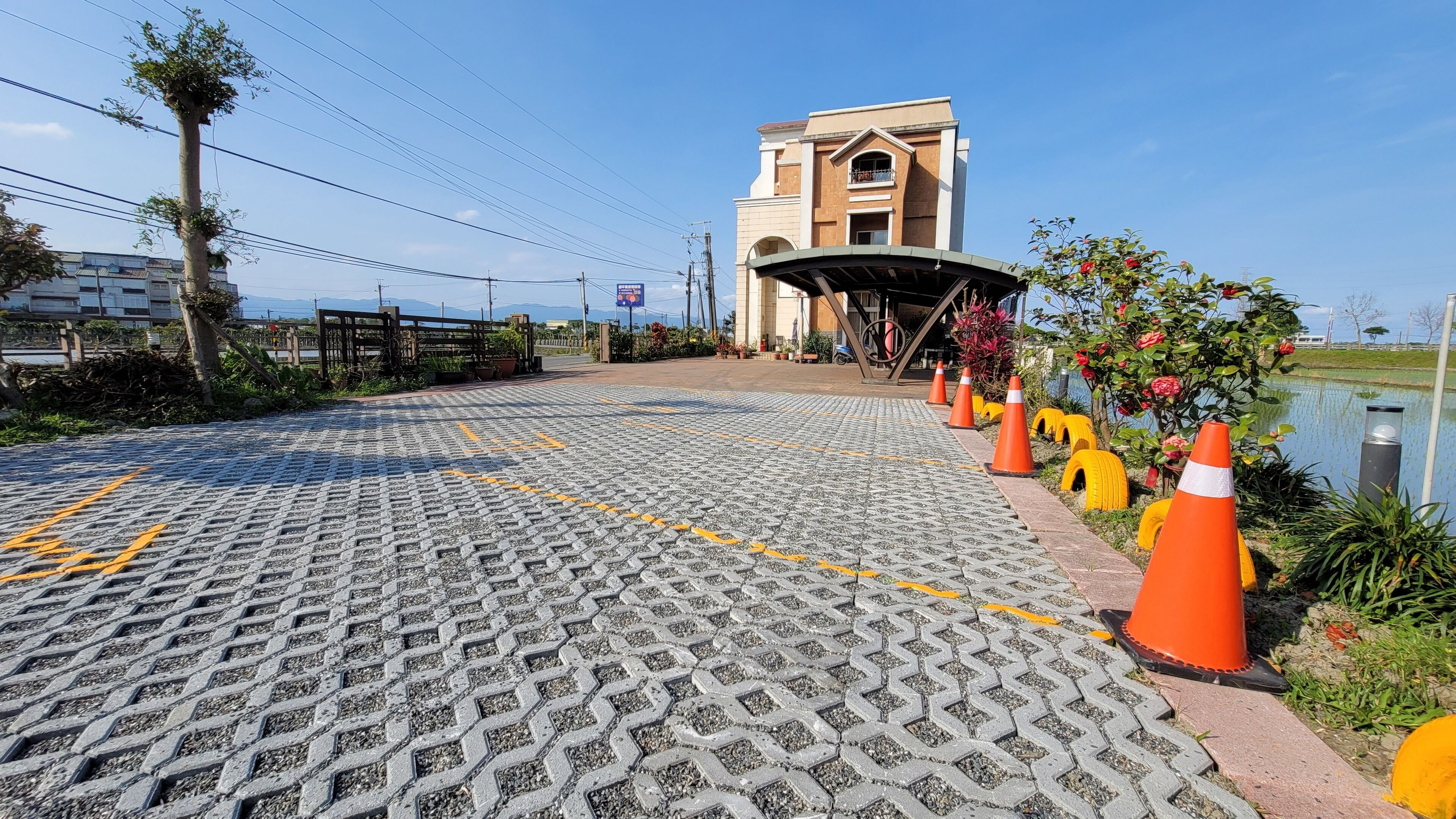 A paved walkway leading to a building with a covered entrance, surrounded by orange traffic cones and potted plants.