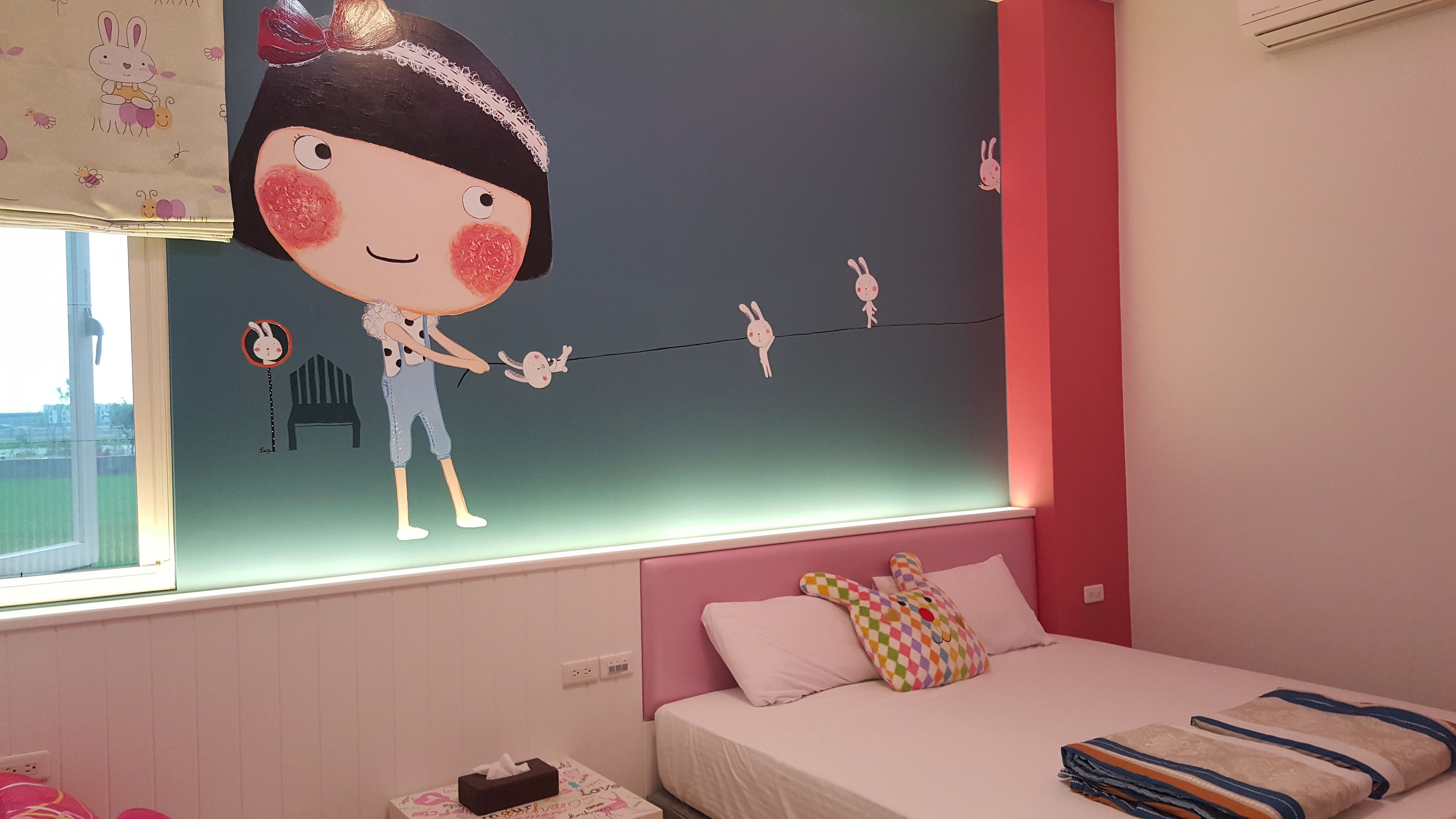 A bedroom with a bed, a window, and a wall with a cartoon character.