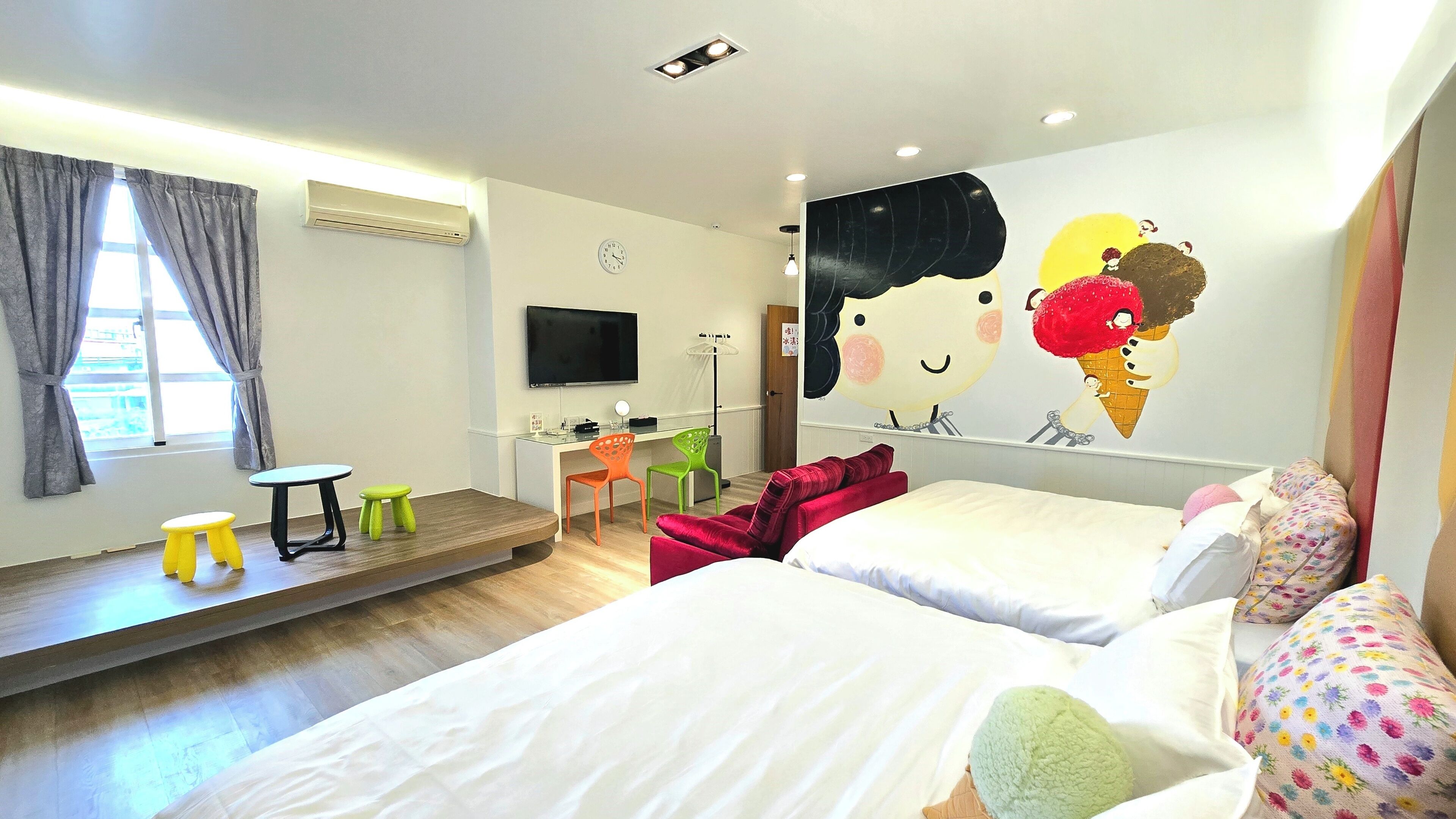 Habitación de hotel con dos camas, un escritorio, una silla, un televisor y un mural grande en la pared.
