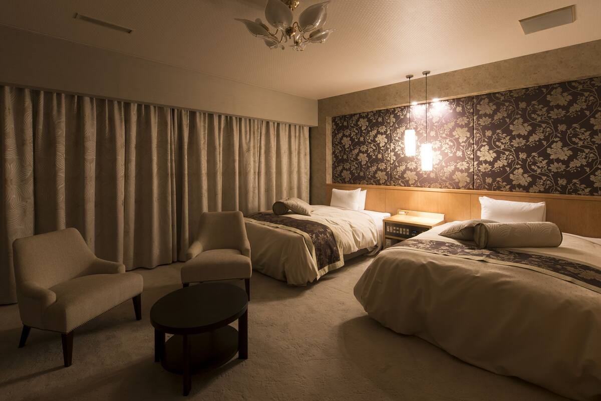 Ett hotellrum med två sängar, en soffa, ett litet bord och en dekorativ väggpanel.