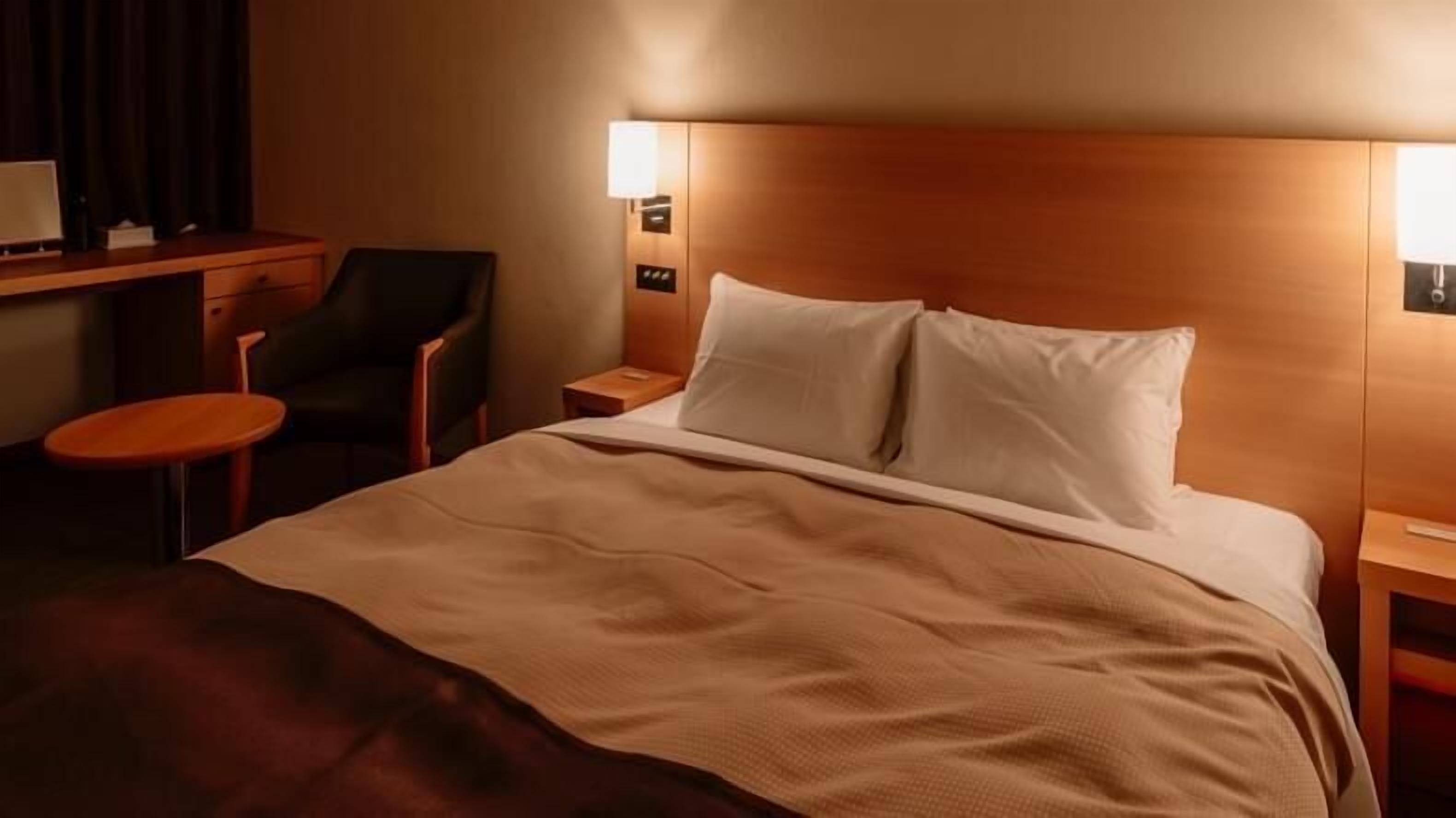 A hotel room with a bed, a desk, a chair, and a nightstand.