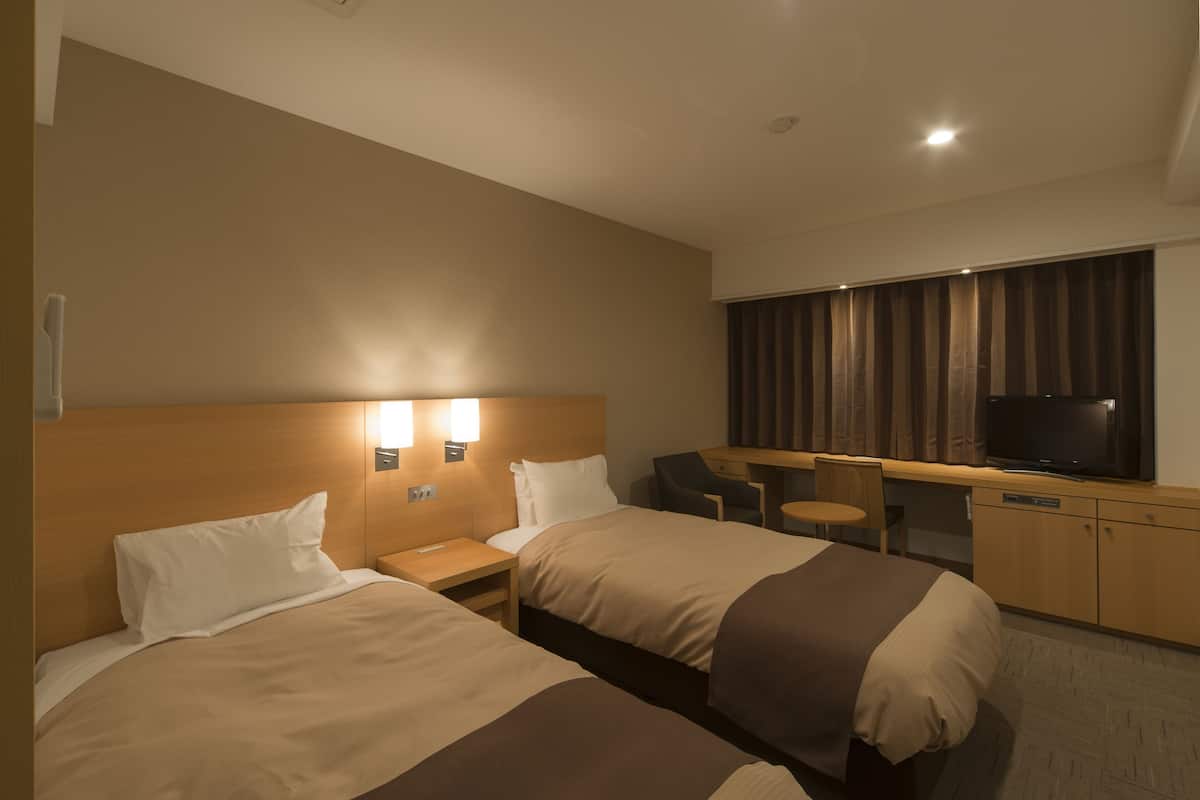 Ett hotellrum med två sängar, ett skrivbord, en tv och ett fönster med gardiner.
