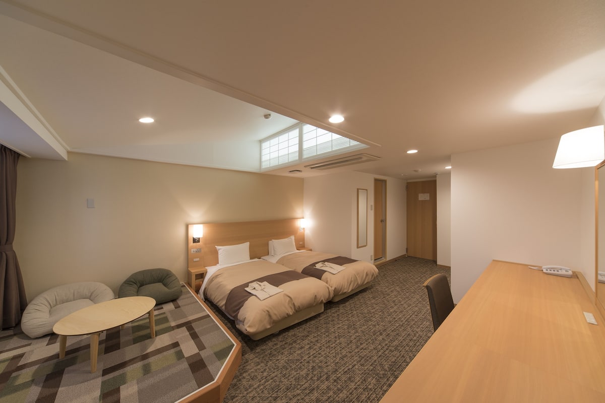 Ett hotellrum med två sängar, ett litet bord, en stol och ett skrivbord.