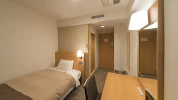 A hotel room with a single bed, a wooden desk, a chair, a mirror, and a door leading to another room.