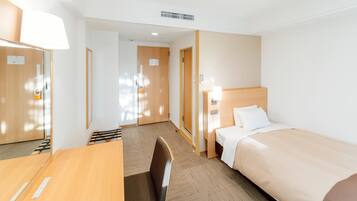 A hotel room with a bed, a desk, a chair, and a door.