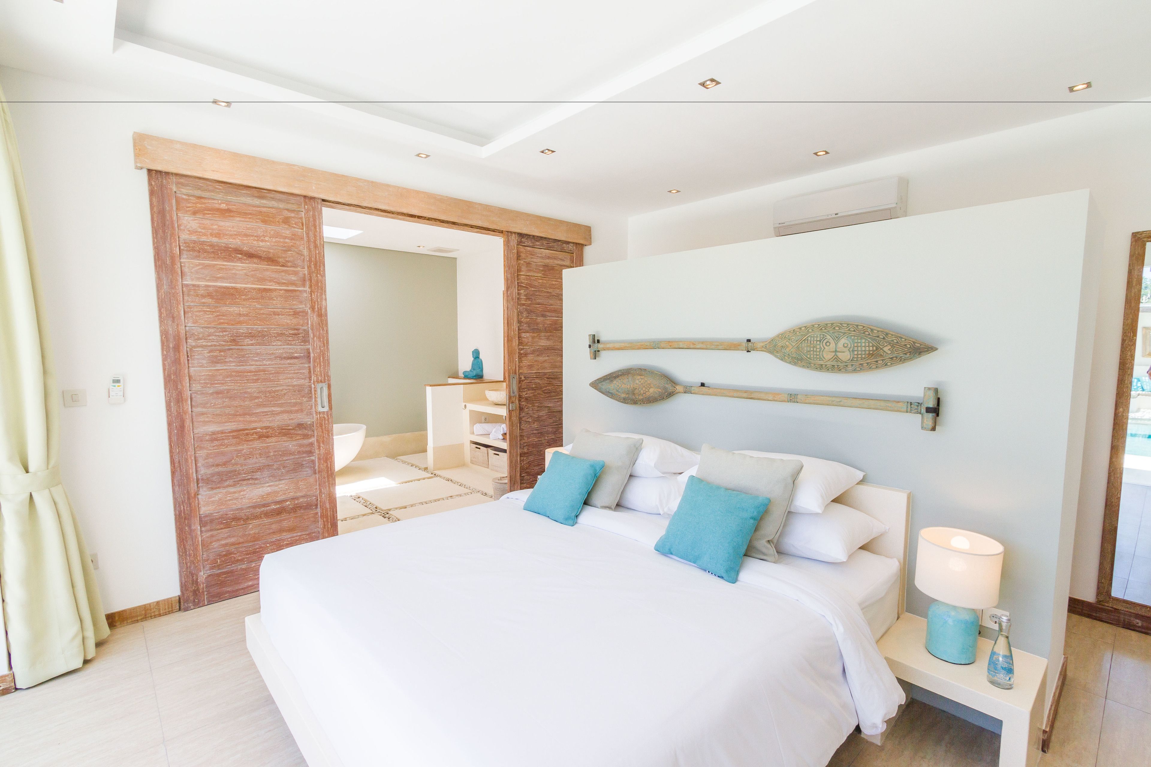 A modern bedroom with a large bed, a wooden door, a bedside table with a lamp, and a decorative wall piece.