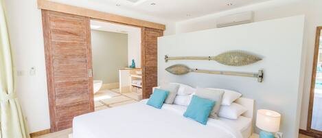 A modern bedroom with a large bed, a wooden door, a bedside table with a lamp, and a decorative wall piece.