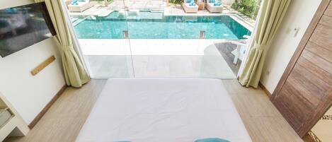 Un dormitorio con una cama grande, televisor y vista a una piscina al aire libre.