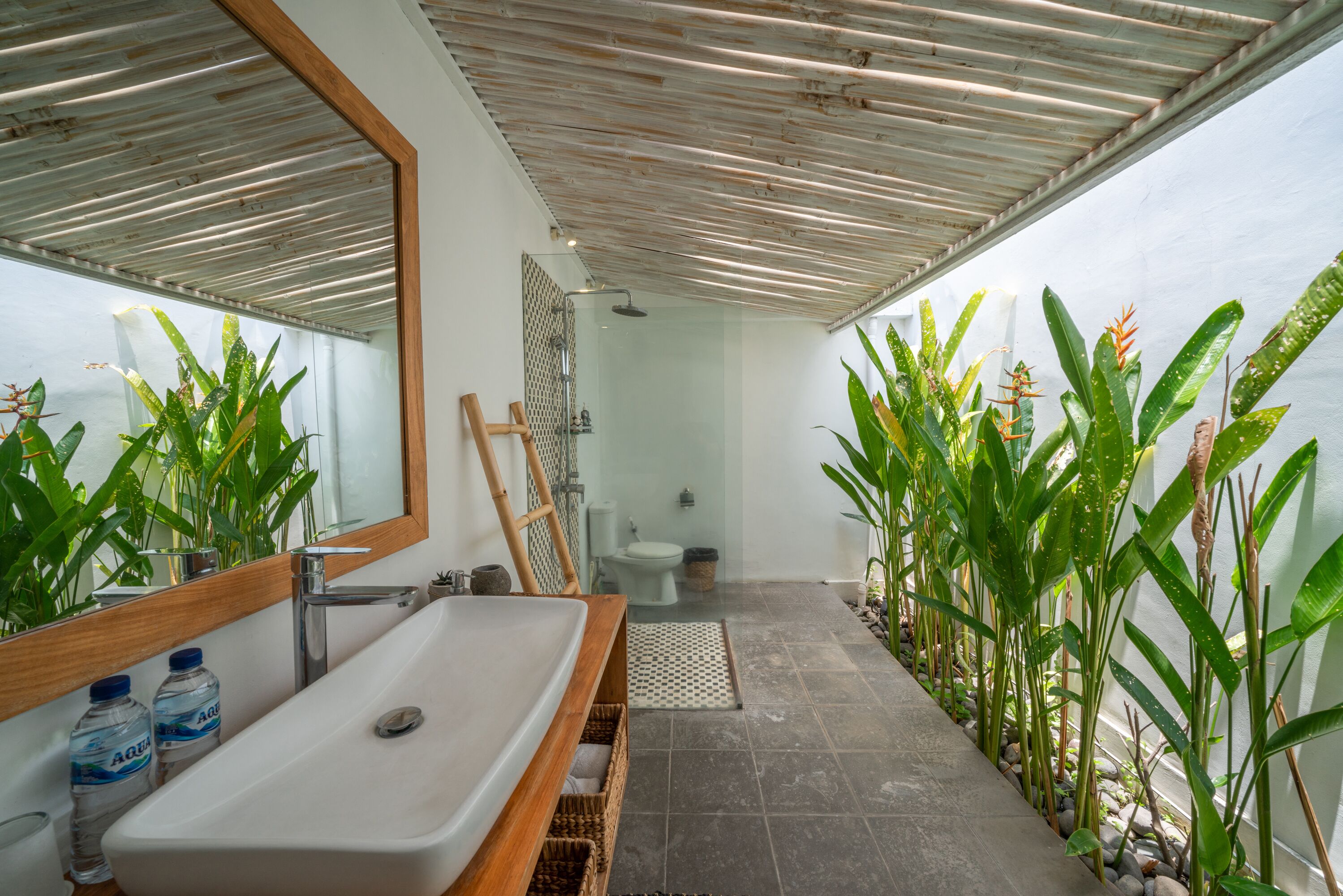 A bathroom with a wooden vanity, a large mirror, a white sink, and a shower area.