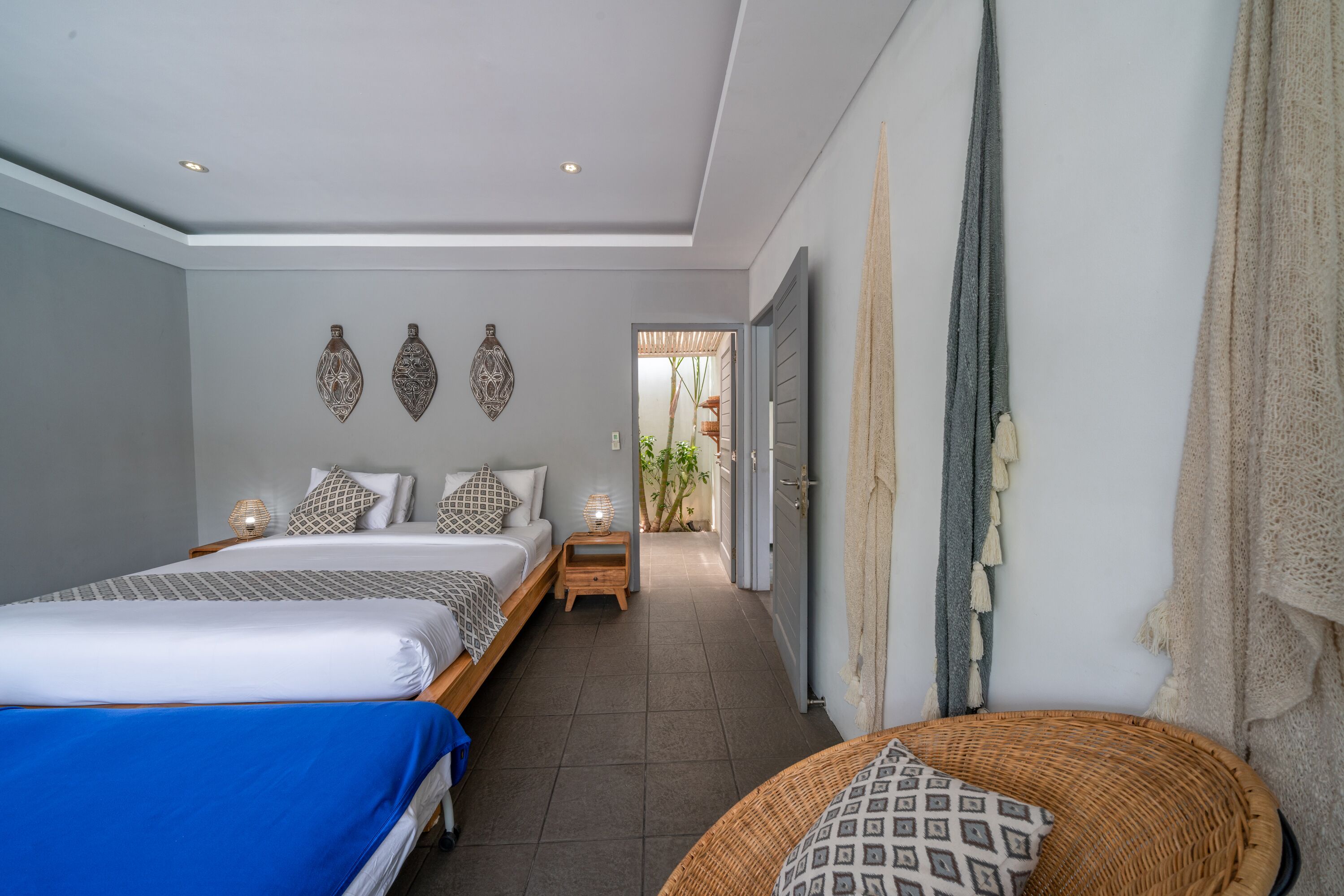A bedroom with two beds, a small table, and a wicker chair.