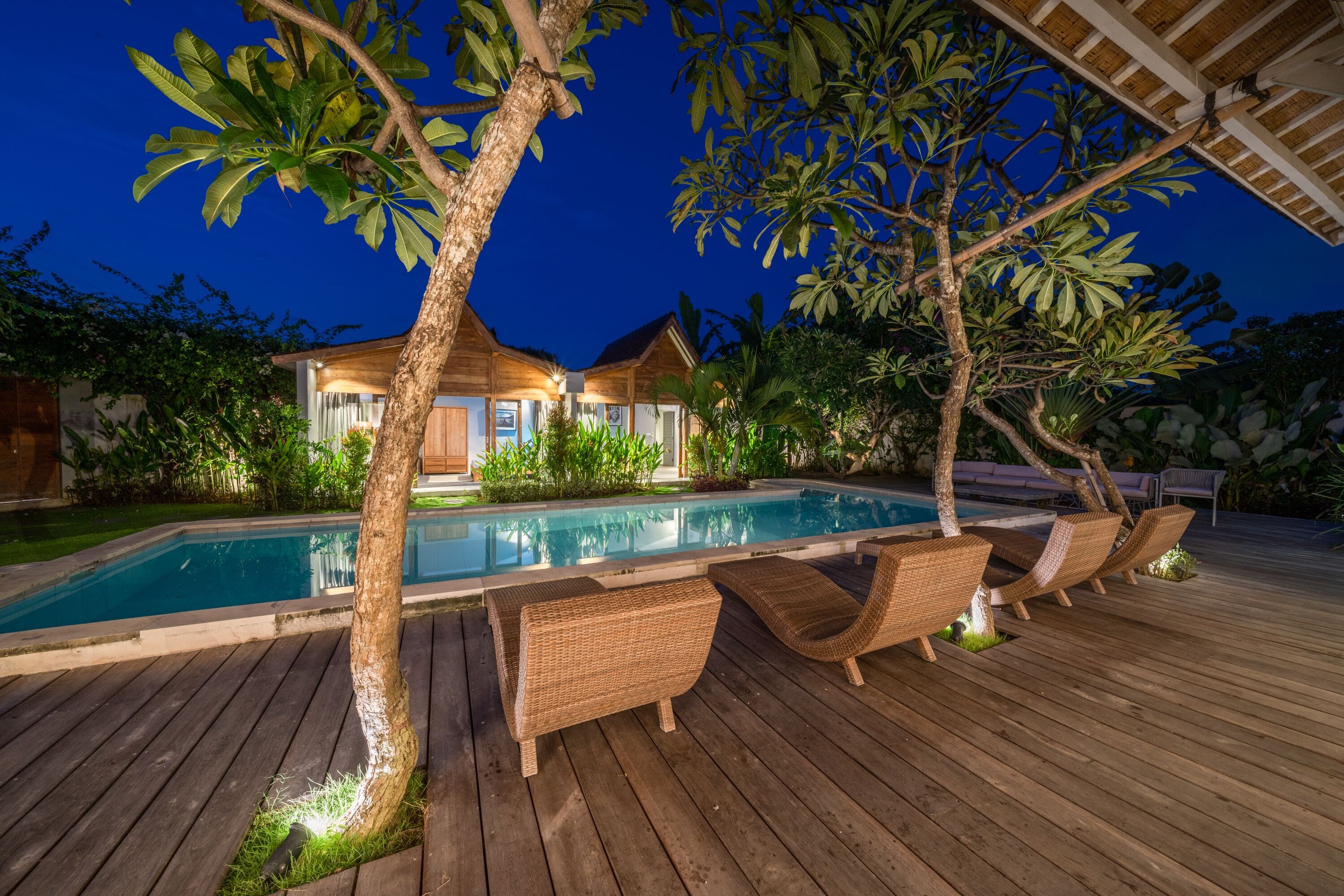 A wooden deck with a pool, lounge chairs, and a house in the background.