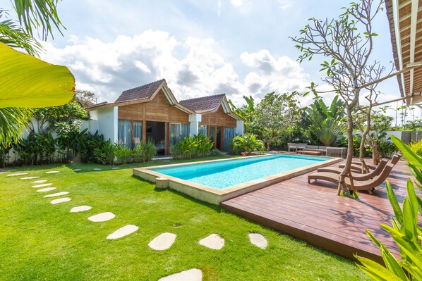 Enjoy a serene garden and pool area with a spacious deck, perfect for relaxation.