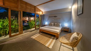 A bedroom with a large bed, a wicker chair, and a view of greenery outside. - Villa Nahema (Seminyak)