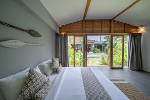 Relax in this serene bedroom with a large bed, sofa, and sliding glass door leading to a pool and lush greenery.