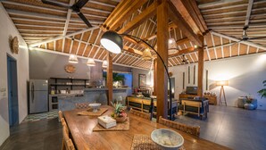 A spacious living area with a wooden dining table, a kitchen in the background, and a ceiling with exposed beams. - Villa Nahema (Seminyak)